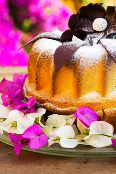 bundt cake on plate decorated with chocolate flowers and garden as background