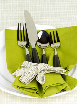 Elegant Table Setting with Fork, Table Knife, Spoon and Dessert Fork into Green Napkin Decorated with Green Checkered Bow on White Plate