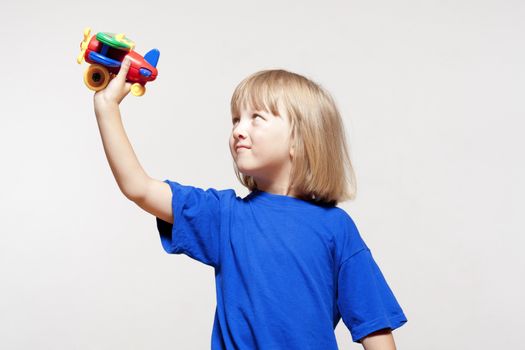 boy with long blond hair playing with toy airplane - isolated on light gray