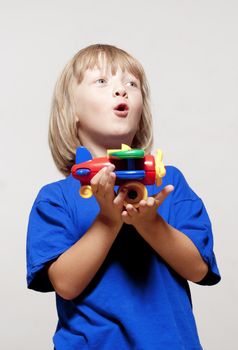 boy with long blond hair playing with toy airplane - isolated on light gray