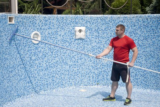 Man in sportswear cleans artificial pool is filled with water