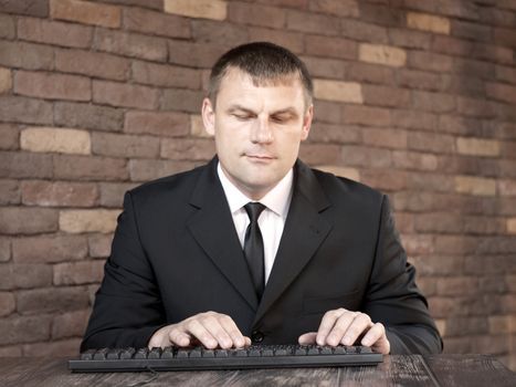 The man in black suit sitting at a desk and looking at the keyboard