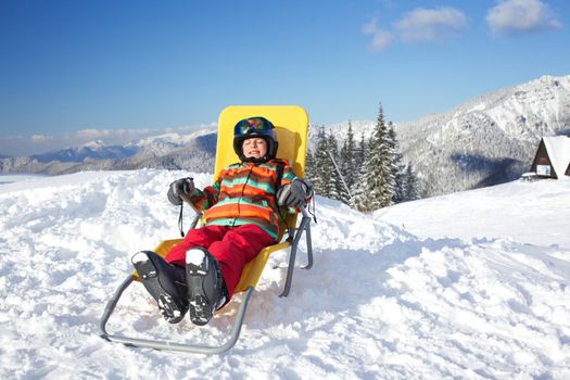 Winter, ski, sun and fun - happy girl skier in winter resort resting in the deck chair