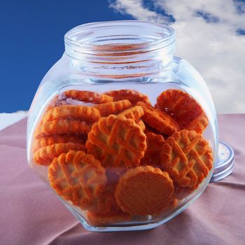 A glass vase of biscuits over a table, with cloudy sky on the background