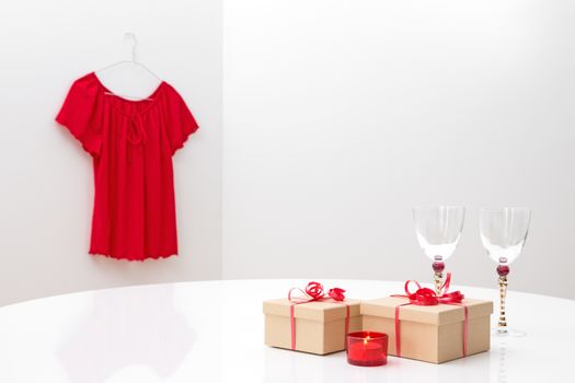 Presents, glasses and candlelight on a table, and red blouse on a hanger.