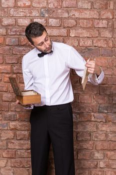 Man standing reading a old document from a wooden box which he is holding in his hand while standing in front of a brick wall