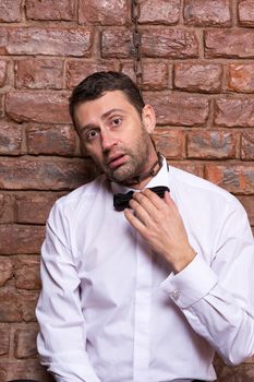 Conceptual image of a desperate handsome businessman in a bow tie standing against a brick wall with a chain around his neck and a disconsolate depressed expression