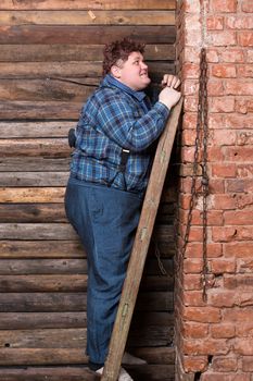 Happy overweight young man standing against a brick wall at the top of a stepladder laughing