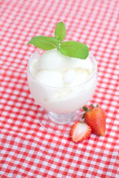 ice cream with mint in a glass bowl and strawberry on plaid fabric