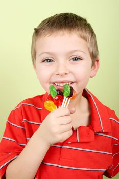 Little blond boy against yellow background eating candy