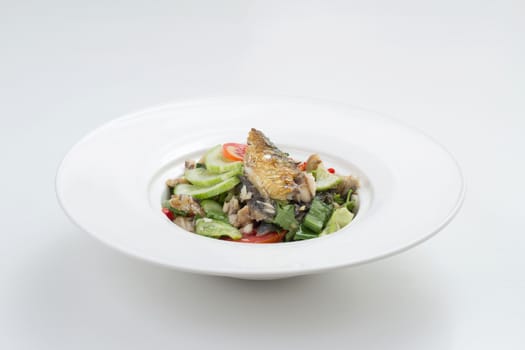 Thai appetizer - spicy mackerel salad with lemon grass, shallots, raw mango, chili and lettuce on a white plate