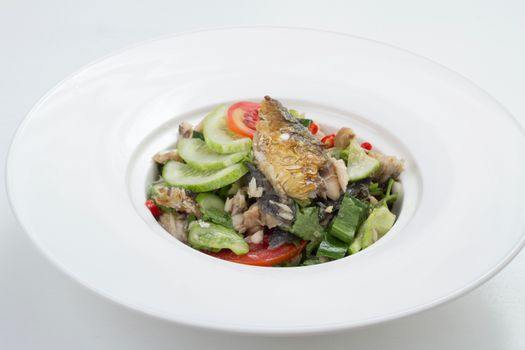 Thai appetizer - spicy mackerel salad with lemon grass, shallots, raw mango, chili and lettuce on a white plate