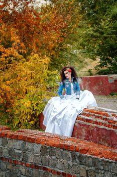 Beautiful bride in wedding dress and denim jacket in autumn park