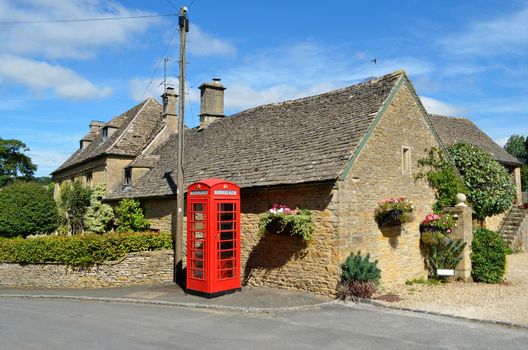 Honey coloured stone houses and a red telephone box in a village in the Cotswolds in rural England.