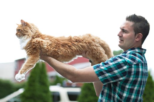 Man holding his cherished purebred Maine Coon cat outright to show his size.  Shallow depth of field.