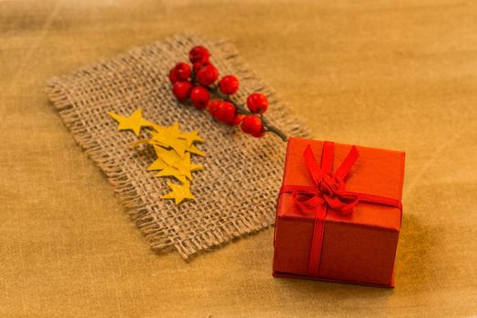 Present box, red berries and rope carpet on golden background