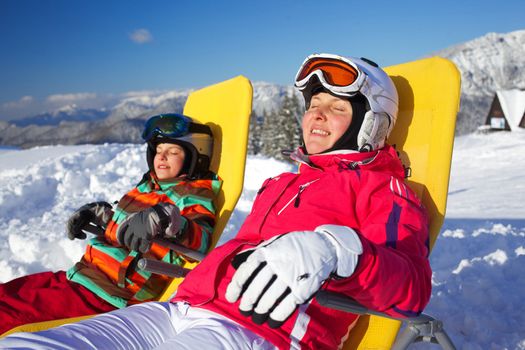 Winter, ski, sun and fun - Portrait of mother with her daughter in winter resort resting in the deck chair