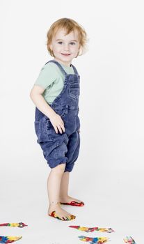 child with painted feet holding trousers up. studio shot in grey background