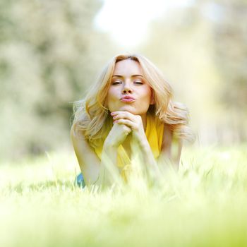 Happy young woman lying on grass and blowing kiss