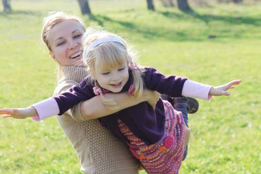 Happy mother making little daughter fly in the spring meadow