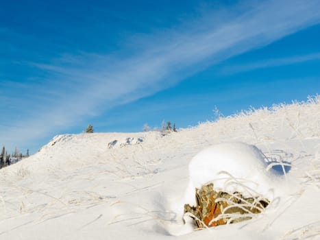 Barren tundra winter landscape scene of snow-covered rocky hillside under blue sky