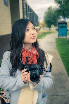 Girl photographer with camera on a public side walk during autumn listening to music