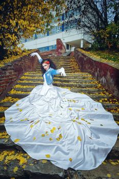 Beautiful bride in magnificent dress stands alone on stairs in autumn day