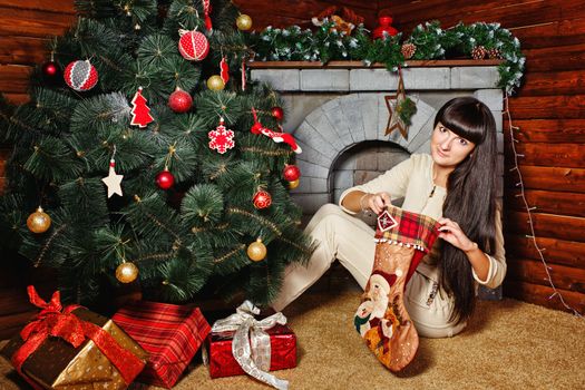 Attractive young woman holding gift and sits near Christmas tree