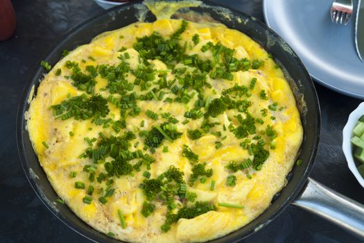 Omelet scrambled eggs with chives and herbs in a frying pan