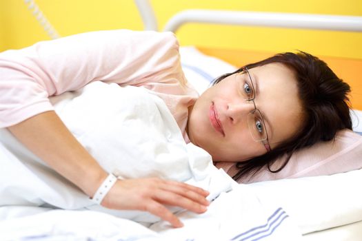 Real people in real situation, smiling middle-aged woman lying in hospital with pneumonia