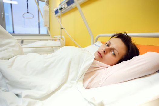 Real people in real situation, sad middle-aged woman lying in hospital with pneumonia