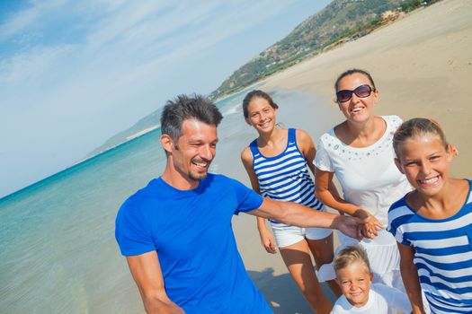 Photo of happy family with three kids running down the beach