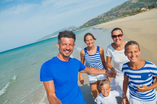 Photo of happy family with three kids running down the beach