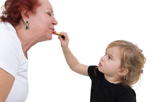 Young girl concentrates on applying lipstick to her grandmother's lips. Studio portrait over white.