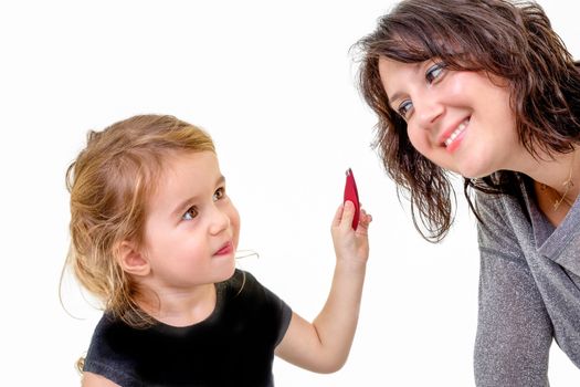 Cute little girl with a playful expression wanting to apply her mothers makeup holding it up in her hand as her mother bends forwards to oblige with a smile, isolated on white