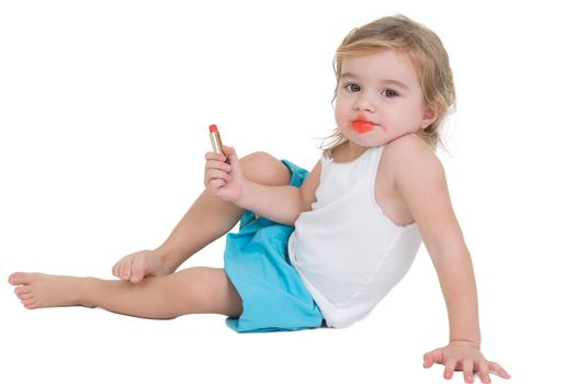 Cute little girl playing with red lipstick sitting on the floor with her mouth smeared in red, isolated on white