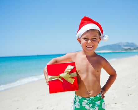Cute little boy in Santa hat with gift on tropical vacation