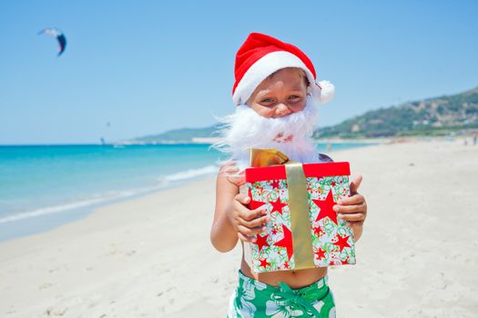 Cute little boy in Santa hat with gift on tropical vacation