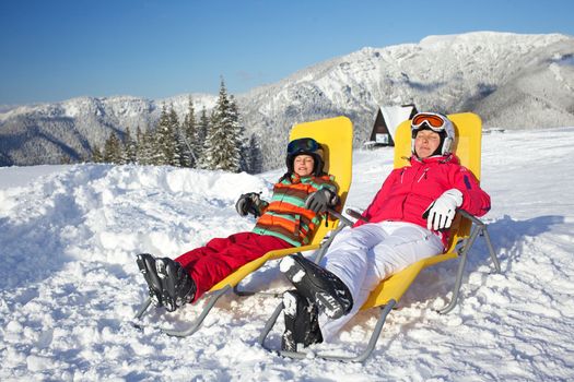 Winter, ski, sun and fun - mother with her daughter in winter resort resting in the deck chair