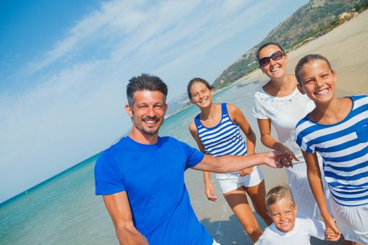 Photo of happy family with three kids running down the beach