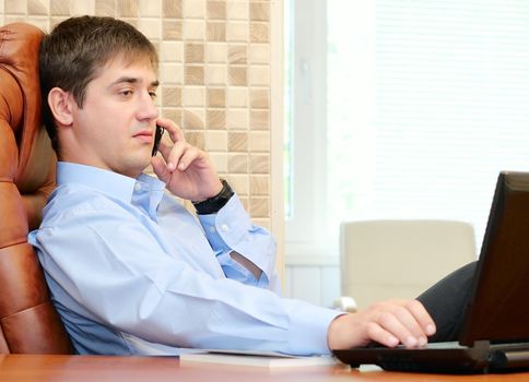 Man in the office talking by phone and loking into laptop