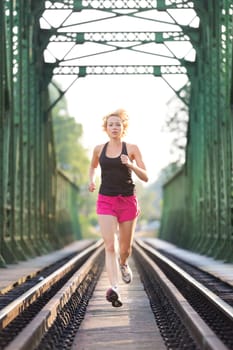 Athlete running on railaway tracks bridge in morning sunrise training for marathon and fitness. Healthy sporty caucasian woman exercising in urban environment before going to work; Active urban lifestyle.