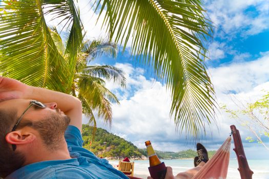 Man relaxing on a tropical beach with a bottle of beer in his hand.