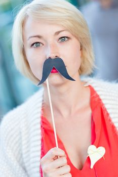 Portrait of girl wearing fake mustache: symbol of Movember, annual, month-long event involving the growing of moustaches during the month of November to raise awareness of men's health issues.