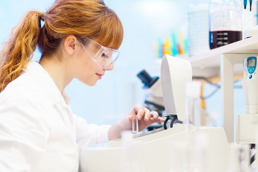 Focused attractive young life science professional measuring the absorbance of the solution in cuvette in the spectrophotometer. Focus on the researcher's face.