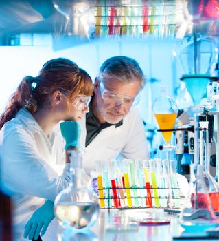 Attractive young female scientist and her senior male supervisor looking at the cell colony grown in the petri dish in the life science research laboratory (bichemistry, genetics, forensics, microbiology..)