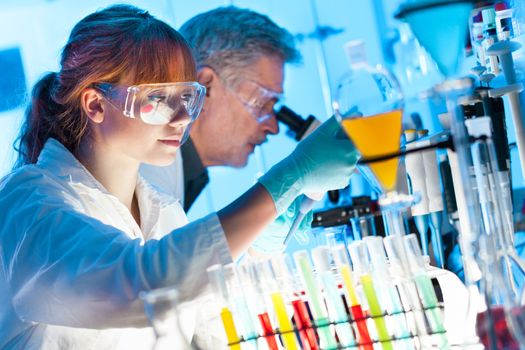 Attractive young female scientist and her senior male supervisor pipetting and microscoping in the life science research laboratory (biochemistry, genetics, forensics, microbiology..)