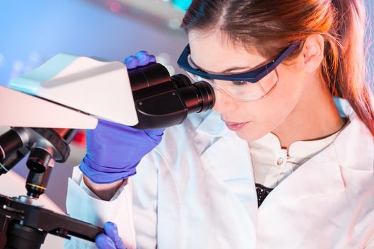 Attractive young scientist looking at the microscope slide in the forensic laboratory.