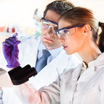 Attractive young scientist and her suprvisor looking at the microscope slide in the forensic laboratory.