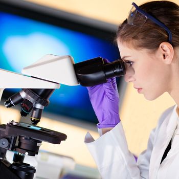 Attractive young scientist looking at the microscope slide in the forensic laboratory.